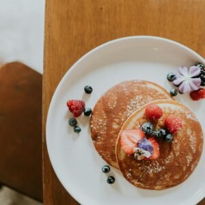 Top-down view of gourmet pancakes with berries and flowers, on a wooden table.